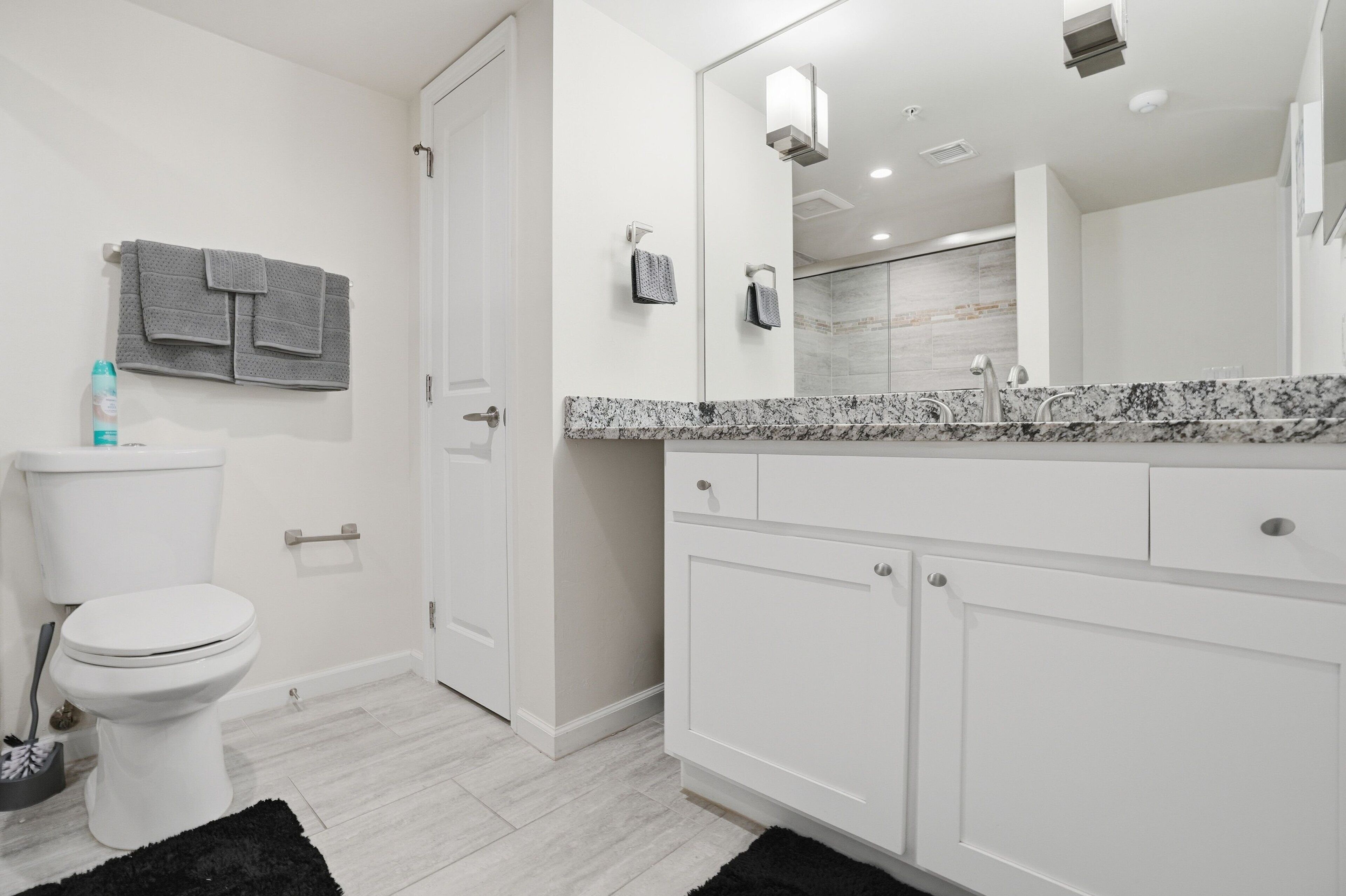 A modern bathroom with a toilet, a sink with a marble countertop, and a large mirror.