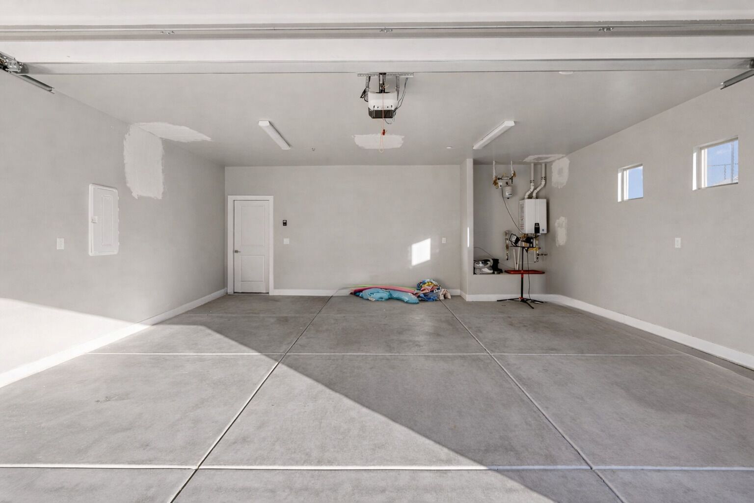 A spacious, unfinished garage with concrete flooring, a door, and a ceiling-mounted projector.