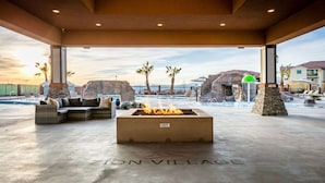 A spacious outdoor area with a fire pit labeled "HOT" and a lounge with wicker furniture. The area is named "ZION VILLAGE" and features a pool and a view of the ocean. - Zion Adventure 6 Bedroom Townhouse (Hurricane)