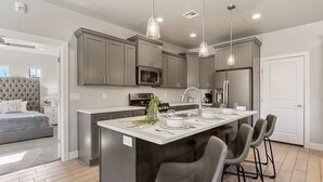 A modern kitchen with grey cabinets, a central island with bar stools, and pendant lighting. - Zion Adventure 6 Bedroom Townhouse (Hurricane)