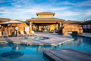 Un área de piscina con sillones de descanso, un jacuzzi y un edificio con porche cubierto.