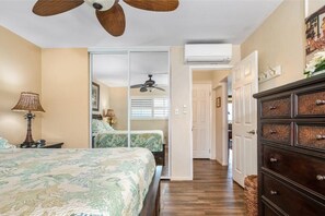 A bedroom with a bed, a ceiling fan, a dresser, and a door leading to another room. - Menehune Shores, #308 2 Bedroom Condo (Kihei)