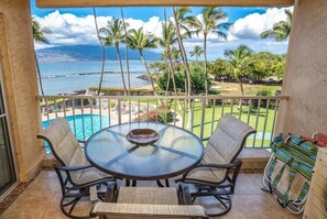 A balcony with a glass table and chairs, overlooking a pool and a view of the ocean. - Menehune Shores, #308 2 Bedroom Condo (Kihei)