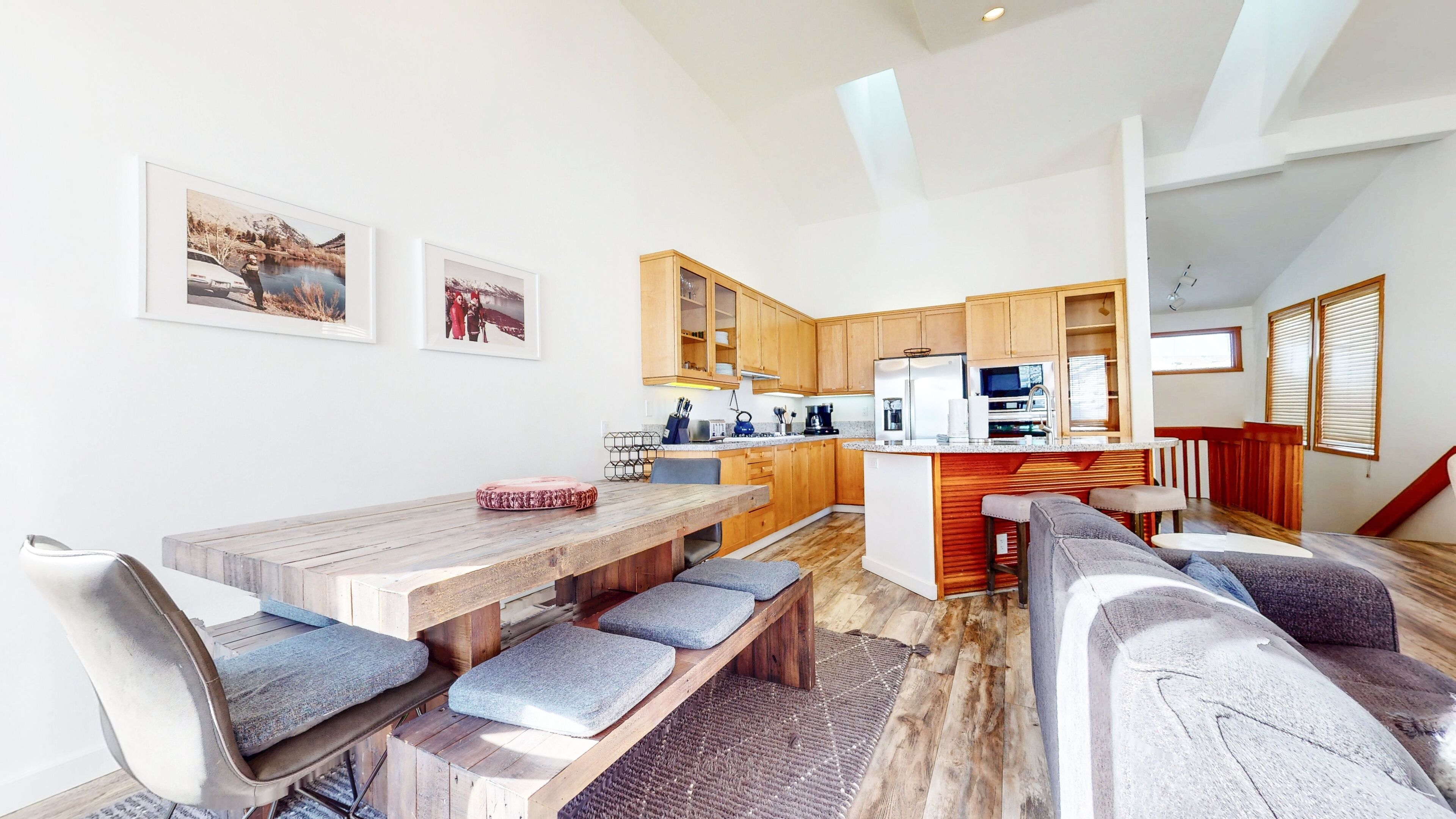 Una cocina moderna con armarios de madera, una isla central y un comedor con una mesa de madera y bancos grises acolchados.