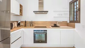 A modern kitchen with white cabinetry, a stainless steel oven, and a window with blinds. - BEAUTIFUL APARTMENT IN RESIDENCE JARDINES DE LOS MENCEYES HEATED SWIMMING POOL (Palm-Mar)