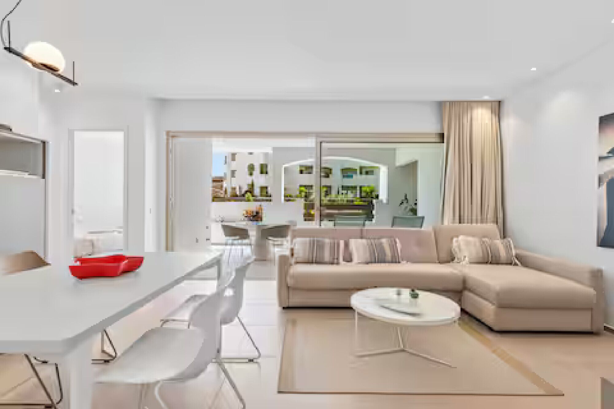 A modern living room with a sofa, a dining table, and a kitchen visible through an open door.