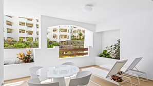 A modern interior with a round dining table, white chairs, and a view of a residential building. - BEAUTIFUL APARTMENT IN RESIDENCE JARDINES DE LOS MENCEYES HEATED SWIMMING POOL (Palm-Mar)