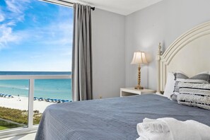 A hotel room with a large bed, a bedside table with a lamp, and a view of the beach and ocean. - Shoreline Towers 2073 2 Bedroom Condo (Destin)