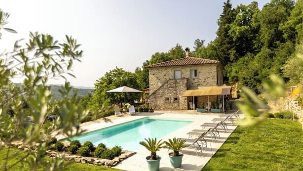 Une maison en pierre avec une piscine, entourée de verdure et sous un ciel dégagé.