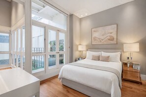 Ein Schlafzimmer mit einem großen Bett, zwei Nachttischen, einem Fenster mit Blick auf Grünflächen.