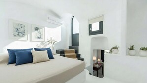 A modern bedroom with a bed, a small seating area, and a fireplace. - Poseidon’s Water Escape Santorini Rooftop Jacuzzi (Santorini)