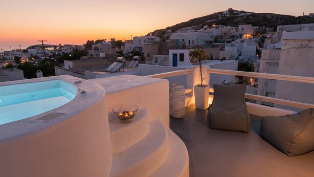 A rooftop terrace with a hot tub, lounge chairs, and a view of a coastal town at sunset. - Poseidon’s Water Escape Santorini Rooftop Jacuzzi (Santorini)
