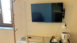 Une petite pièce bien éclairée, équipée d’un bureau, d’une chaise et d’un téléviseur fixé au mur.
