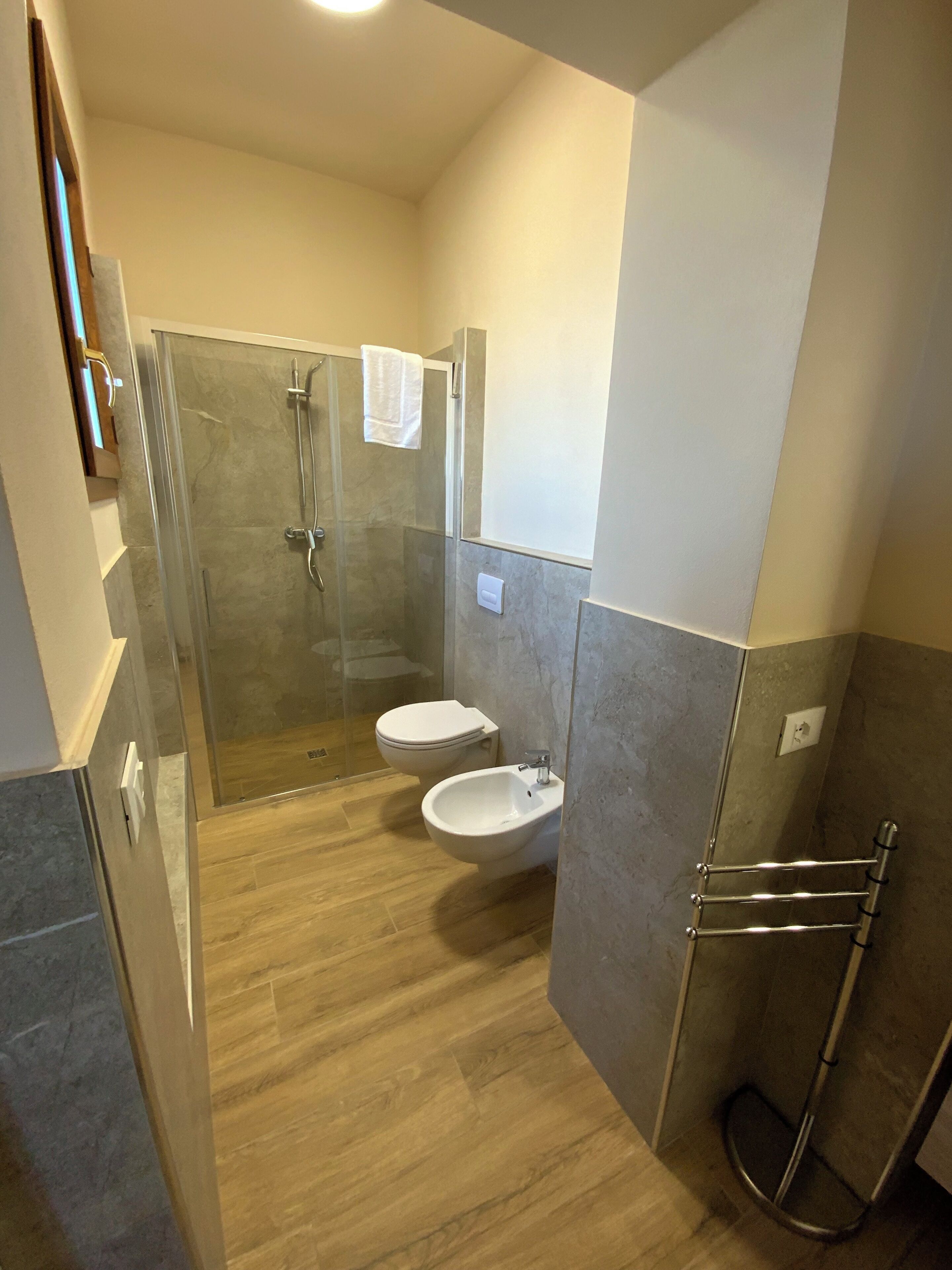 Un baño moderno con ducha acristalada, dos inodoros y un bidé.