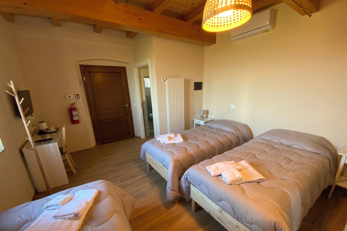 A room with two beds, a wooden floor, a wooden ceiling, a small desk, and a white wall.