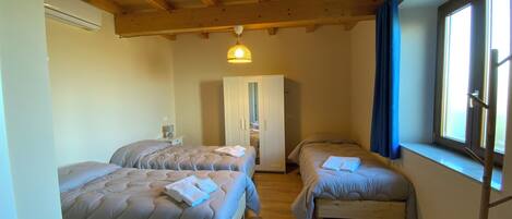 Un dormitorio con dos camas, vigas de madera en el techo, un armario y una ventana con cortinas.