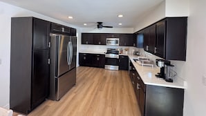 A modern kitchen with dark cabinetry, stainless steel appliances, and a wooden floor.