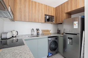 A modern kitchen with wooden cabinets, a microwave, a washing machine, a refrigerator, and a sink. - Urbana Domus Cabrera 401 (Buenos Aires)