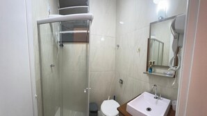 A bathroom with a glass shower enclosure, a white toilet, and a sink with a mirror above it. - kitnet petropolis (Petrópolis)