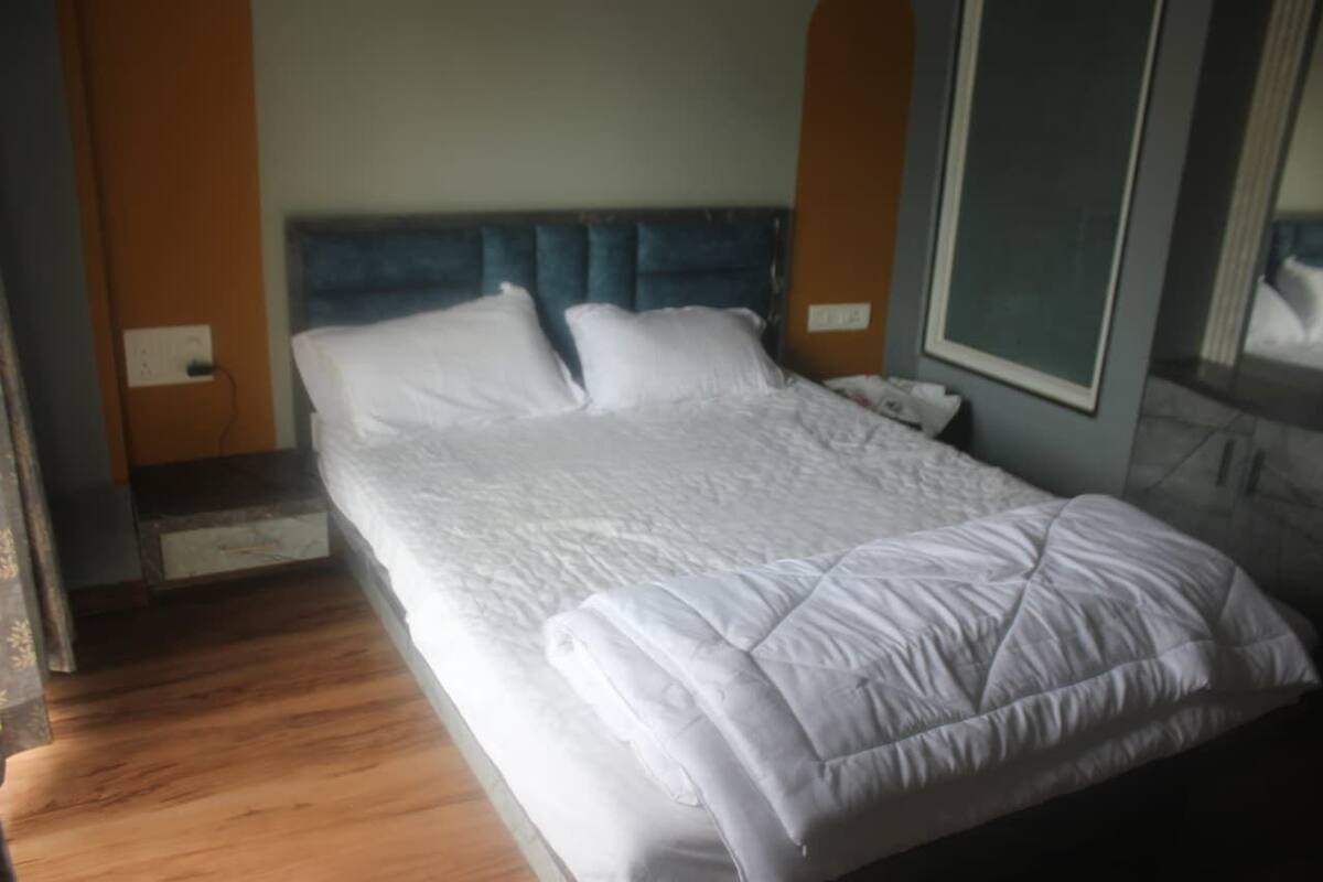 Una cama bien hecha con cabecera azul, suelo de madera y espejo fijado a la pared.