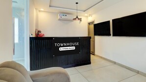 Ein Empfangsbereich mit einem schwarzen Empfangstresen mit der Aufschrift "TOWNHOUSE Company Serviced", einer deckenmontierten Klimaanlage und einem wandmontierten Flachbildfernseher.