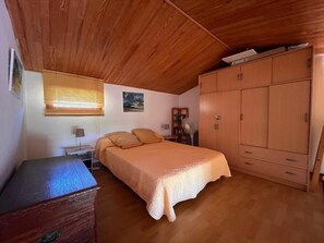 A bedroom with a wooden ceiling, a bed with an orange bedspread, a wooden wardrobe, and a desk with a lamp. - Waterfront paradise (Vico)