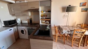 Une cuisine compacte équipée d’un lave-linge, d’un four à micro-ondes et d’un évier. Un coin repas avec une table et des chaises est également disponible.