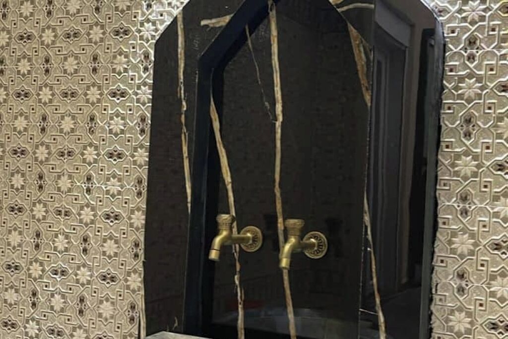 Une salle de bain avec un mur en marbre foncé, deux robinets en laiton et un pare-chocs mural en carreaux décoratifs.