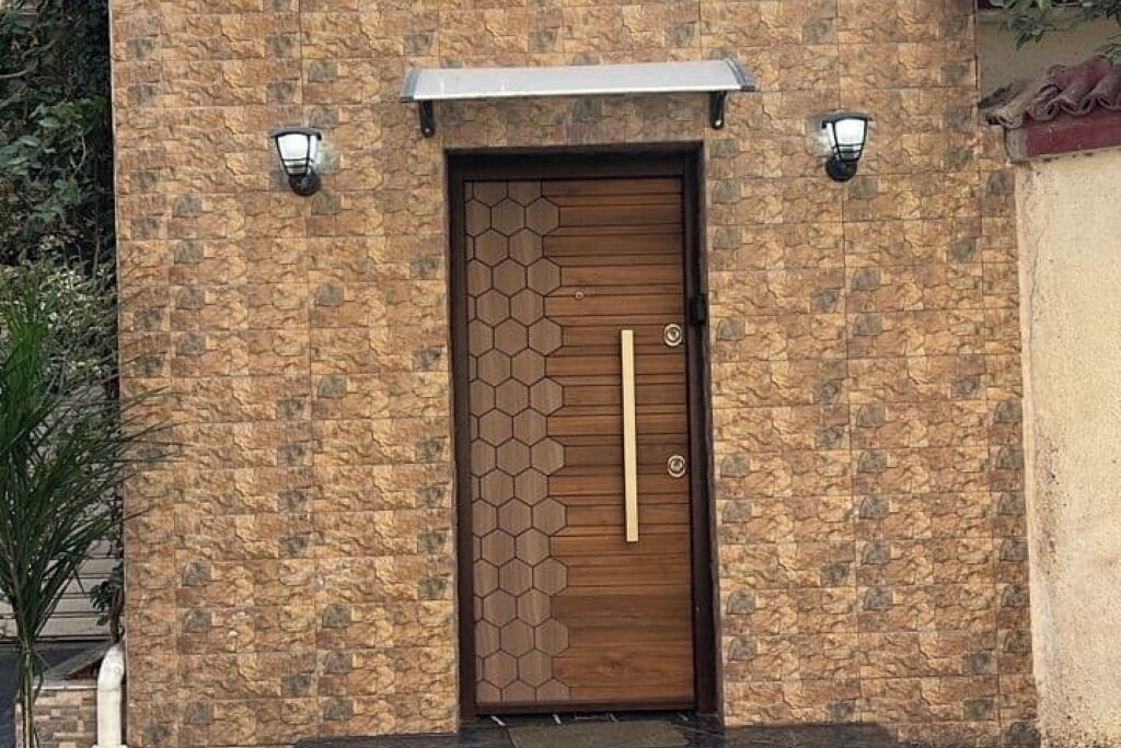 A wooden door with a hexagonal pattern, flanked by two wall-mounted lights, set in a stone wall.