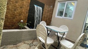 A patio with a stone wall, a small waterfall feature, and a table with chairs.