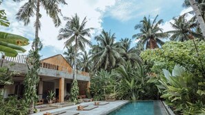 A pool area with wooden deck and lounge chairs, surrounded by tropical plants and palm trees. - Surfing Temple Boutique Hotel (General Luna)
