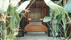 A bedroom with a bed, a wooden ceiling, and large tropical plants. - Surfing Temple Boutique Hotel (General Luna)