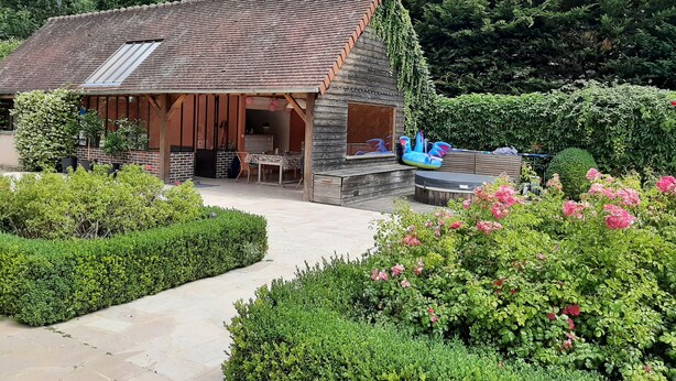 Un edificio rústico de madera con techo inclinado, un patio con mesa y sillas, y una piscina pequeña.