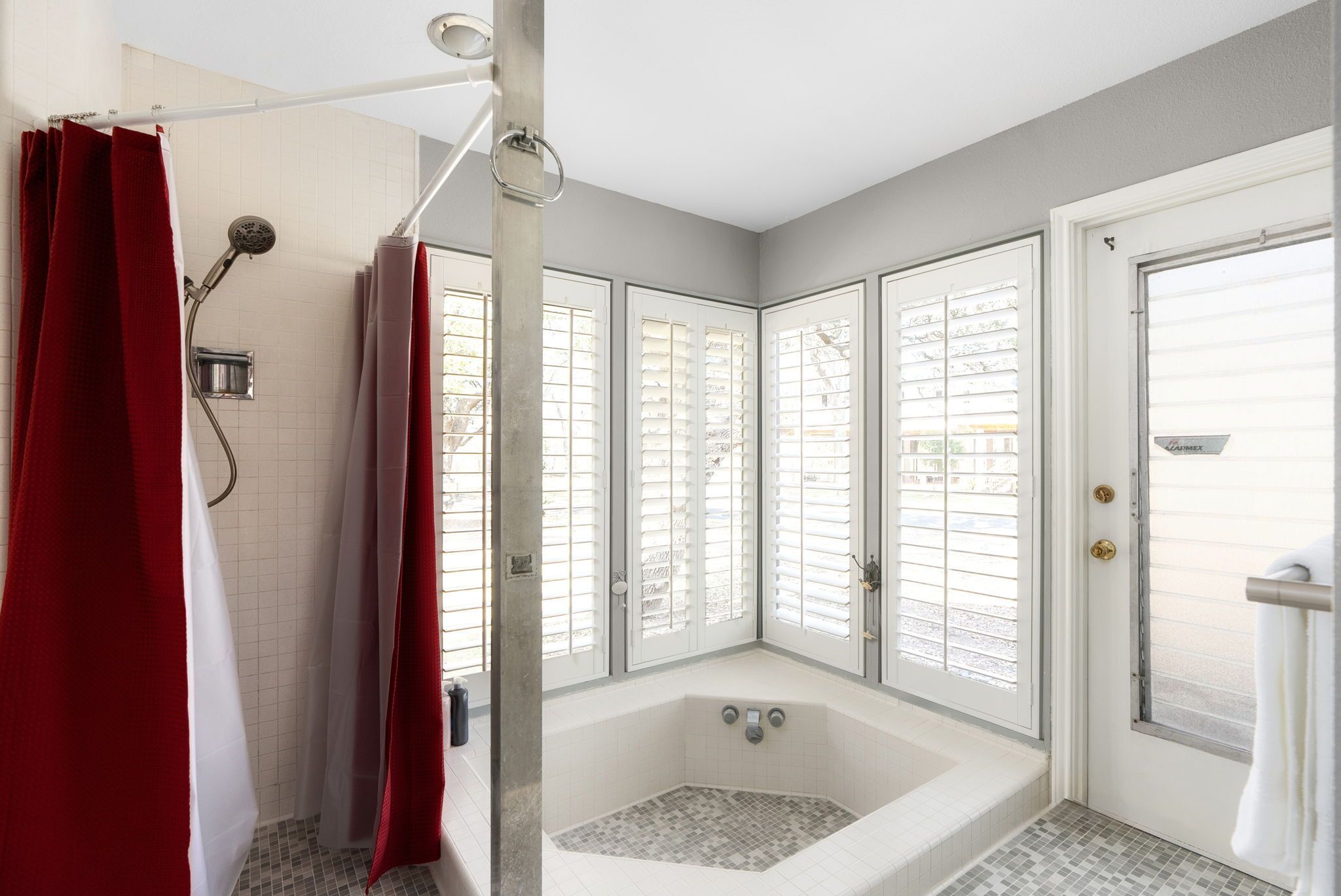 Une salle de bain avec une baignoire, une douche et une fenêtre avec des stores.