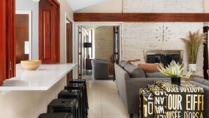 A modern living room with a fireplace, a sofa, and a coffee table. There are suitcases stacked in the corner, suggesting a temporary stay. - The Mid-Century Modern House - Long Term Available (Seguin)