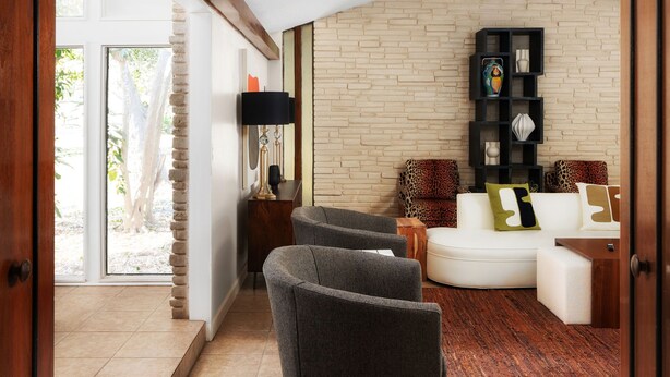 A modern living room with a stone wall, a white sofa, and a black shelving unit. - The Mid-Century Modern House - Long Term Available (Seguin)