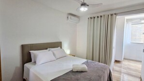 A bedroom with a bed, a ceiling fan, and a window with curtains. - COOND0124 - Edifício Solarius (Salvador)