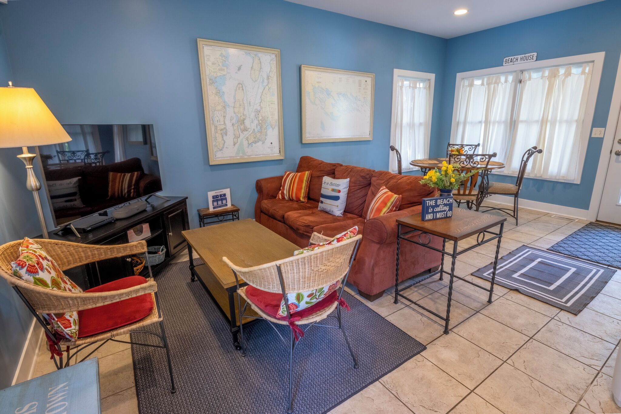 A living room with a brown sofa, a wooden coffee table, wicker chairs, a TV, and framed maps on the wall.