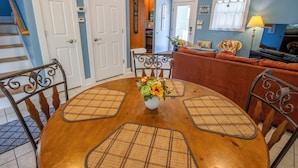 A dining area with a round wooden table, woven placemats, and a vase of flowers. There are two doors, one leading to a kitchen and another to a living area. - Beachwalk Resort Guest House w/Pool, Beach, More (Michigan City)