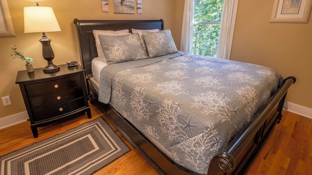 A bedroom with a bed, nightstand, lamp, and artwork on the walls. - Beachwalk Resort Guest House w/Pool, Beach, More (Michigan City)