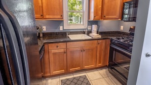 A kitchen with wooden cabinets, a black stove, and a window with a view of greenery. - Beachwalk Resort Guest House w/Pool, Beach, More (Michigan City)