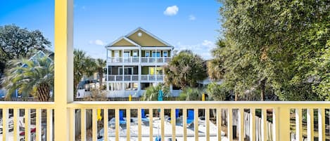 A two-story house with a balcony, surrounded by trees and a pool area.