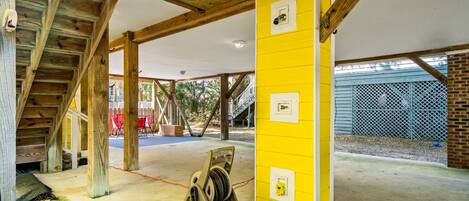 A covered outdoor area with wooden beams, a yellow wall with electrical outlets, and a concrete floor.