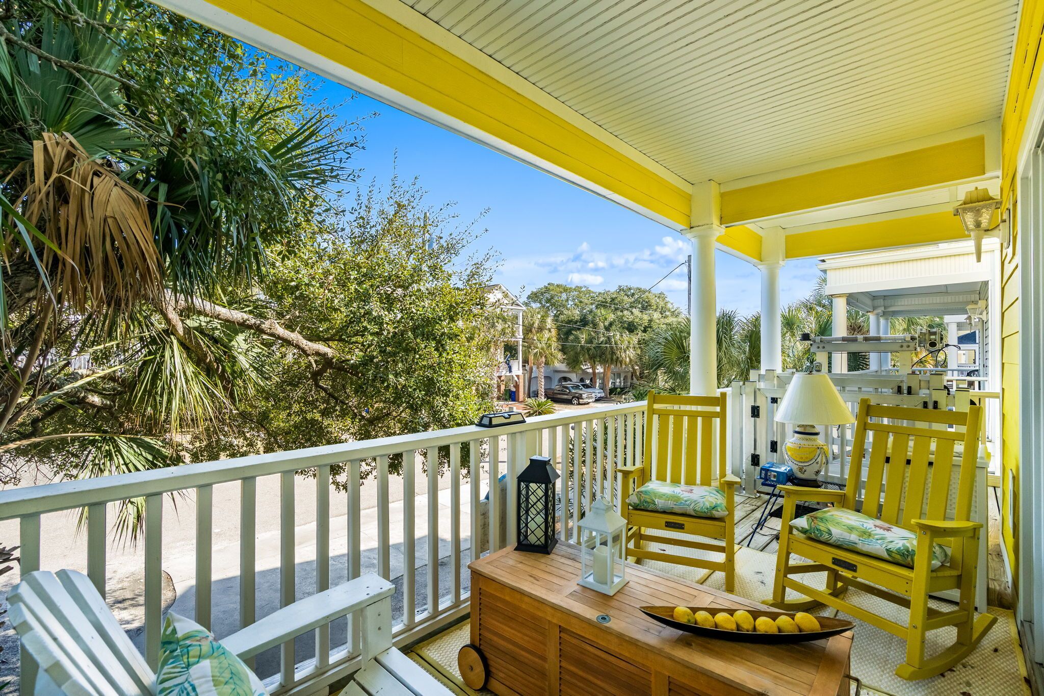 A yellow porch with a wooden table, two rocking chairs, and a white railing.