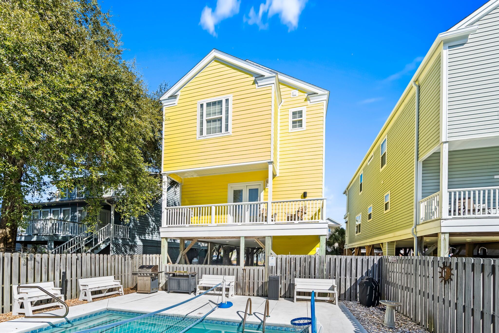 A two-story yellow house with a balcony, a fenced backyard, and a swimming pool.