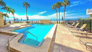 Una piscina con vista al océano, rodeada de palmeras y sillas de descanso.