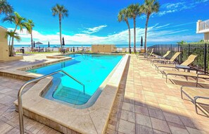 A swimming pool with a view of the ocean, surrounded by palm trees and lounge chairs. - Two Bedroom Two Bath Direct Gulf Front Penthouse (Redington Shores)