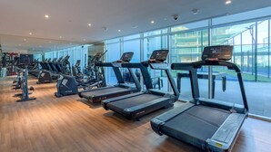 Un gimnasio moderno con cintas de correr, máquinas de pesas y un amplio ventanal con vistas al exterior del edificio.