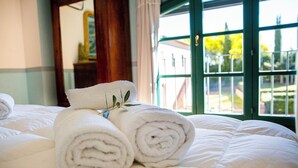 A neatly made bed with rolled white towels and a view of a building through a green-framed window. - Agriturismo gli Archi (Fauglia)