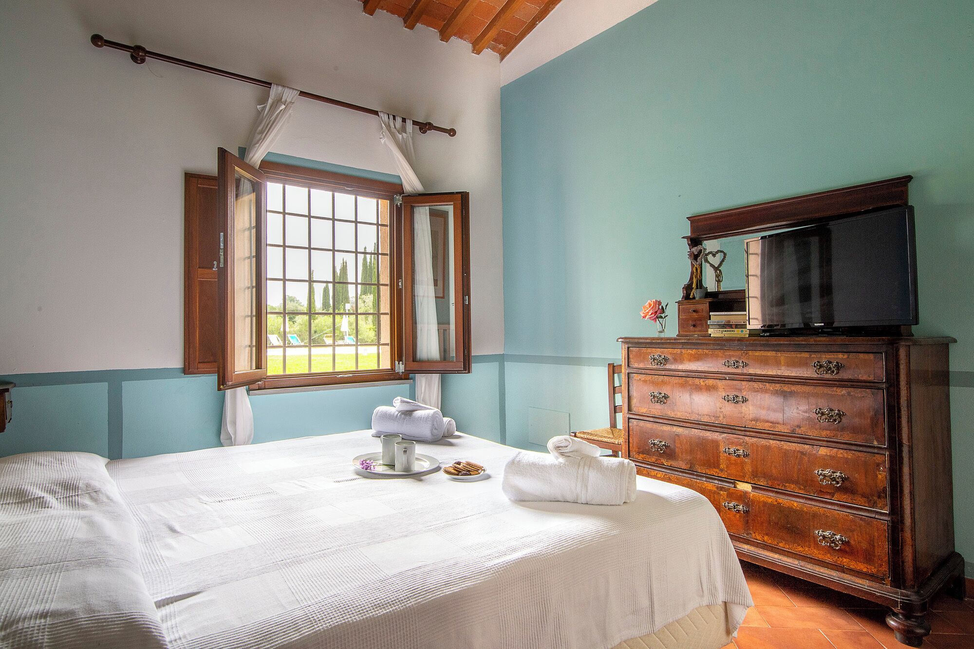 A bedroom with a bed, a dresser, a television on top of the dresser, and a window with curtains.